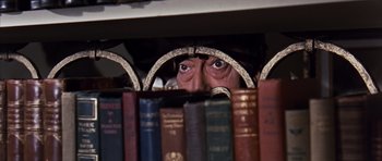 Movie still from “Gambit” (1966), directed by Ronald Neame – A man peeking over a shelf with a bunch of books; Close Up shot, High angle