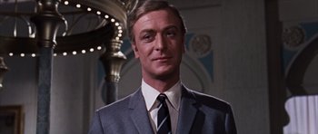 Movie still from “Gambit” (1966), directed by Ronald Neame – A person wearing a suit and tie; Close Up shot, Low angle