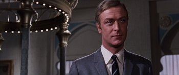 Movie still from “Gambit” (1966), directed by Ronald Neame – A person wearing a suit and tie; Close Up shot, Low angle