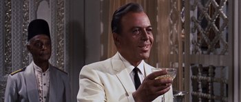Movie still from “Gambit” (1966), directed by Ronald Neame – A man in a white suit holding a glass of wine; Close Up shot, Low angle