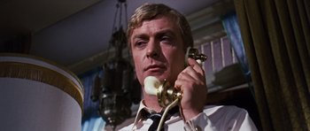 Movie still from “Gambit” (1966), directed by Ronald Neame – A man holding a phone up to his ear while wearing a tie; Close Up shot, Low angle
