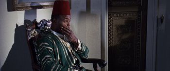 Movie still from “Gambit” (1966), directed by Ronald Neame – A man wearing a fez sitting in a chair with his hand to his face; Close Up shot, Over the shoulder angle