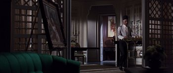 Movie still from “Gambit” (1966), directed by Ronald Neame – A man standing in a living room next to a painting; Wide shot, Low angle