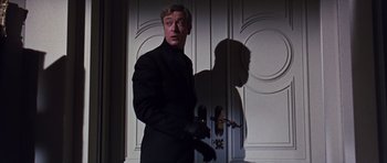 Movie still from “Gambit” (1966), directed by Ronald Neame – A man standing in front of a white door; Medium shot, Low angle