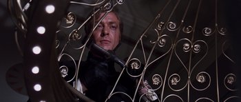 Movie still from “Gambit” (1966), directed by Ronald Neame – A man holding a wrench in front of an ornate metal fence; Medium shot, Low angle