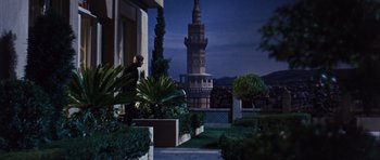 Movie still from “Gambit” (1966), directed by Ronald Neame – A man standing on a balcony in front of a clock tower at night; Extreme Wide shot, Low angle