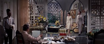 Movie still from “Gambit” (1966), directed by Ronald Neame – A woman standing in front of a dining room table; Wide shot, High angle