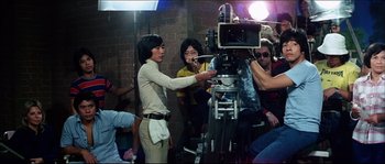 Movie still from “Game of Death” (1978), directed by Robert Clouse – A group of people standing around a video camera; Wide shot, Over the shoulder angle