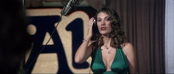 Movie still from “Game of Death” (1978), directed by Robert Clouse – A woman in a green dress is listening to a microphone; Medium shot, Low angle