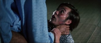 Movie still from “Game of Death” (1978), directed by Robert Clouse – A man is holding his face and neck in his hands; Close Up shot, Over the shoulder angle