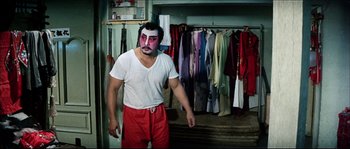 Movie still from “Game of Death” (1978), directed by Robert Clouse – A man in a white t - shirt and red pants standing in front of clothes; Medium shot, Over the shoulder angle