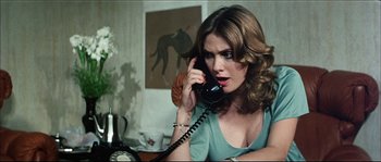 Movie still from “Game of Death” (1978), directed by Robert Clouse – A woman talking on a phone while sitting at a desk; Close Up shot, High angle