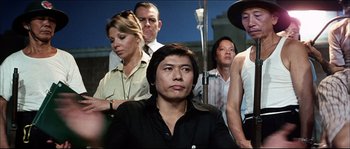 Movie still from “Game of Death” (1978), directed by Robert Clouse – A group of people standing around a man in a black shirt; Medium shot, Over the shoulder angle