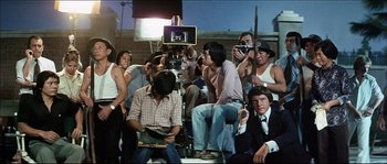 Movie still from “Game of Death” (1978), directed by Robert Clouse – A group of people sitting on a chair in front of a camera; Wide shot, High angle