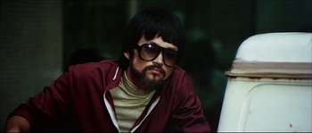 Movie still from “Game of Death” (1978), directed by Robert Clouse – A man with long hair and a beard wearing sunglasses and a maroon jacket; Close Up shot, Low angle
