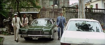 Movie still from “Game of Death” (1978), directed by Robert Clouse – A man in a suit and tie next to a green car; Wide shot, Low angle
