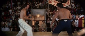 Movie still from “Game of Death” (1978), directed by Robert Clouse – Two men in a boxing ring facing each other in front of a crowd; Wide shot, Over the shoulder angle