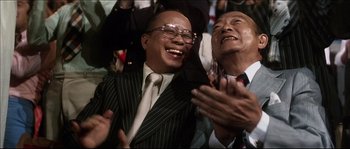 Movie still from “Game of Death” (1978), directed by Robert Clouse – Two men laughing and clapping in a crowd of people; Close Up shot, High angle
