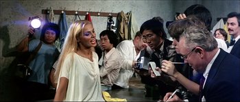 Movie still from “Game of Death” (1978), directed by Robert Clouse – A group of people sitting around a table with a woman in a white dress; Medium shot, Over the shoulder angle