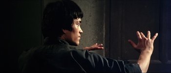 Movie still from “Game of Death” (1978), directed by Robert Clouse – A man sitting in front of a wall with his hand up to his face; Medium shot, Low angle