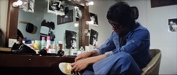 Movie still from “Game of Death” (1978), directed by Robert Clouse – A man sitting in front of a mirror putting on a pair of shoes; Medium shot, Low angle