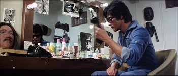 Movie still from “Game of Death” (1978), directed by Robert Clouse – A man sitting in front of a mirror holding a pair of scissors; Medium shot, Over the shoulder angle
