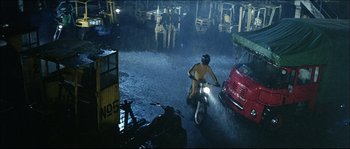 Movie still from “Game of Death” (1978), directed by Robert Clouse – A man riding a motorcycle down a street in the rain; Extreme Wide shot, High angle
