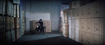 Movie still from “Game of Death” (1978), directed by Robert Clouse – A man riding a motorcycle in a room filled with boxes; Wide shot, High angle