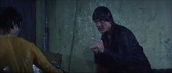 Movie still from “Game of Death” (1978), directed by Robert Clouse – A man in a black jacket is holding his fist up; Medium shot, Low angle