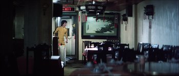 Movie still from “Game of Death” (1978), directed by Robert Clouse – A man standing in front of a television in a room; Wide shot, Over the shoulder angle