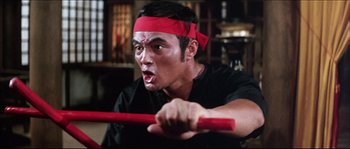 Movie still from “Game of Death” (1978), directed by Robert Clouse – A man with a red headband is holding a red stick; Close Up shot, Low angle