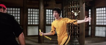 Movie still from “Game of Death” (1978), directed by Robert Clouse – A man holding a banana in a room; Medium shot, Low angle