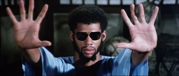 Movie still from “Game of Death” (1978), directed by Robert Clouse – A person wearing sunglasses with their hands up; Close Up shot, Low angle