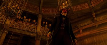 Movie still from “Gangs of New York” (2002), directed by Martin Scorsese – A man standing in front of an audience with a cage hanging from the ceiling; Wide shot, Low angle