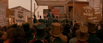 Movie still from “Gangs of New York” (2002), directed by Martin Scorsese – A group of men in top hats sitting in front of an american flag; Wide shot, Low angle
