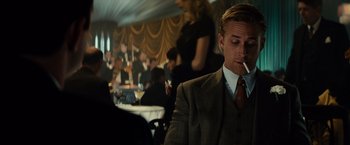 Movie still from “Gangster Squad” (2013), directed by Ruben Fleischer – A man smoking a cigarette in a suit and tie in front of a crowd; Medium shot, Over the shoulder angle