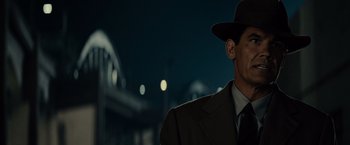 Movie still from “Gangster Squad” (2013), directed by Ruben Fleischer – A man wearing a suit and a hat standing in front of a bridge at night; Close Up shot, Over the shoulder angle