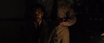 Movie still from “Gangster Squad” (2013), directed by Ruben Fleischer – A man in a suit and tie holding a knife in front of a police officer; Medium shot, Over the shoulder angle