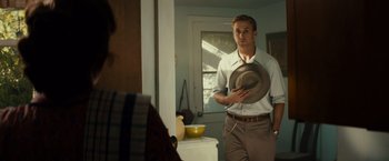 Movie still from “Gangster Squad” (2013), directed by Ruben Fleischer – A man in a white dress shirt and brown pants standing in front of a mirror holding a hat; Medium shot, Over the shoulder angle