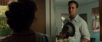 Movie still from “Gangster Squad” (2013), directed by Ruben Fleischer – A man is holding a hat in front of a bowl of food; Medium shot, Over the shoulder angle