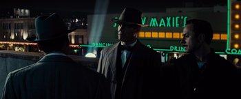 Movie still from “Gangster Squad” (2013), directed by Ruben Fleischer – A man wearing a hat and a suit standing in front of a building; Medium shot, Low angle