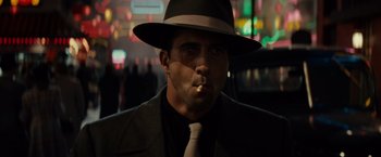 Movie still from “Gangster Squad” (2013), directed by Ruben Fleischer – A man wearing a hat and smoking a cigarette in front of a car; Close Up shot, Low angle
