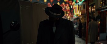 Movie still from “Gangster Squad” (2013), directed by Ruben Fleischer – A man in a suit and hat standing in front of lights; Medium shot, Over the shoulder angle
