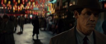 Movie still from “Gangster Squad” (2013), directed by Ruben Fleischer – A man wearing a hat standing on a sidewalk; Close Up shot, Over the shoulder angle