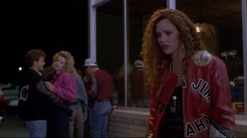 Movie still from “Gas Food Lodging” (1992), directed by Allison Anders – A woman in a red jacket standing in front of a building; Medium shot, Over the shoulder angle