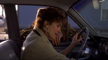 Movie still from “Gas Food Lodging” (1992), directed by Allison Anders – A woman sitting in the driver's seat of a car while looking at her cell phone; Close Up shot, Over the shoulder angle