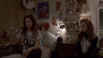 Movie still from “Gas Food Lodging” (1992), directed by Allison Anders – A woman sitting on a bed next to a wall of pictures; Medium shot, High angle