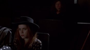 Movie still from “Gas Food Lodging” (1992), directed by Allison Anders – A woman wearing a hat sitting in front of a projector screen; Medium shot, Over the shoulder angle