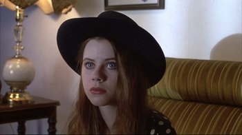 Movie still from “Gas Food Lodging” (1992), directed by Allison Anders – A woman wearing a black hat sitting on a couch; Close Up shot, Low angle