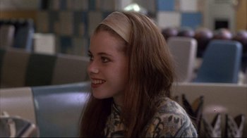 Movie still from “Gas Food Lodging” (1992), directed by Allison Anders – A girl with a headband smiles for the camera; Close Up shot, Over the shoulder angle